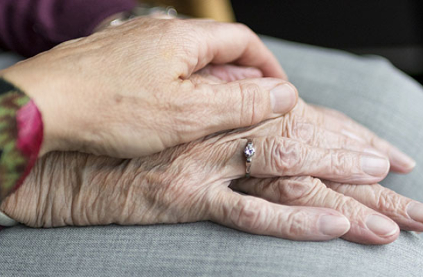 Eine Hand gelegt auf eine zweite Hand. Die zweite Hand ist eine faltige Hand einer älteren Frau.