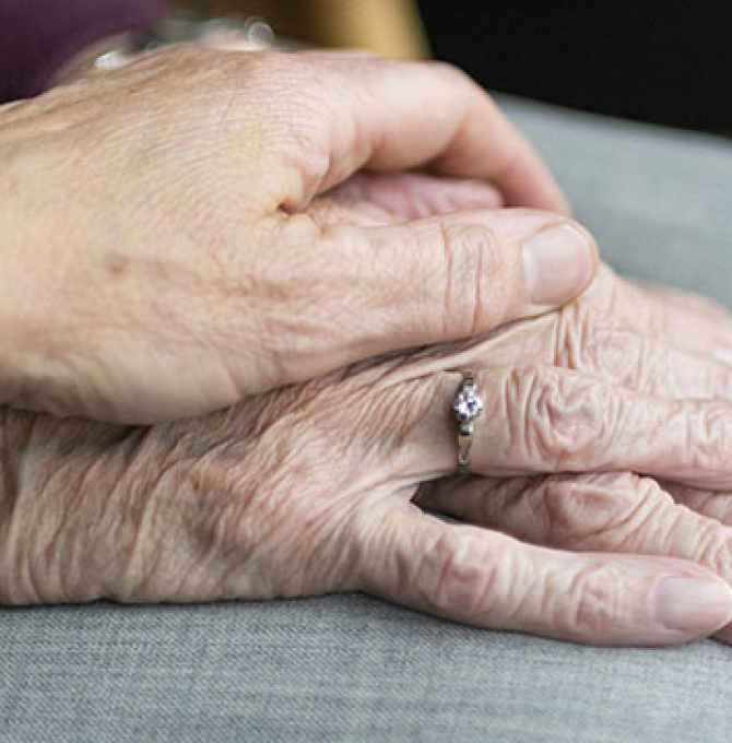 Eine Hand gelegt auf eine zweite Hand. Die zweite Hand ist eine faltige Hand einer älteren Frau.